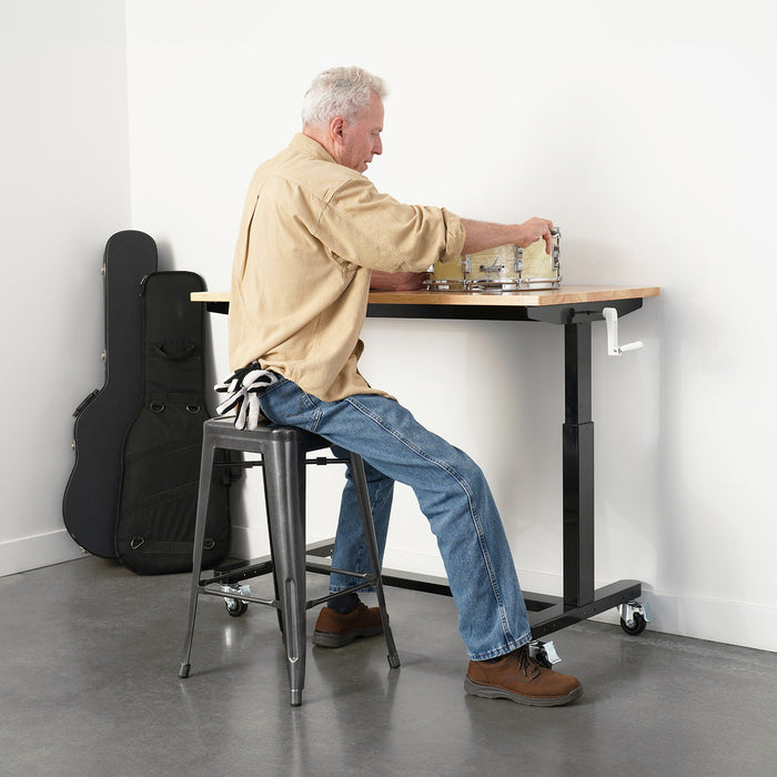 Man sitting on a stool at a workbench working on musical instruments.