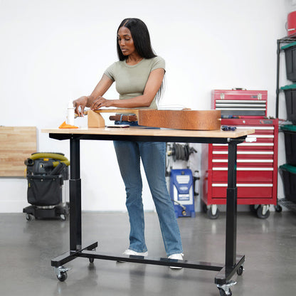 Woman working on a guitar at a standing height workbench in a workshop.